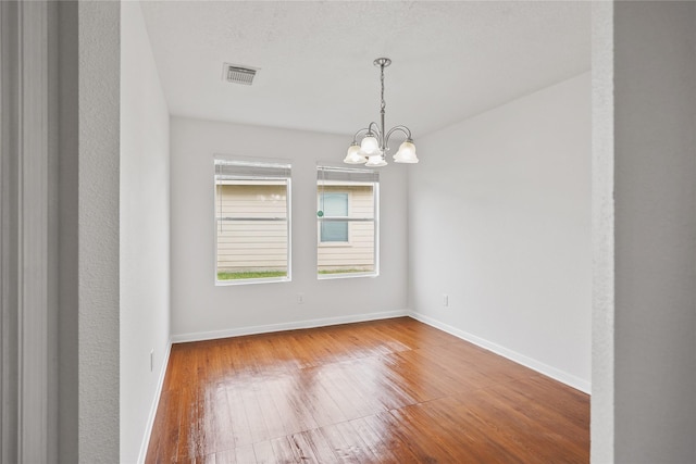 spare room with hardwood / wood-style flooring and an inviting chandelier