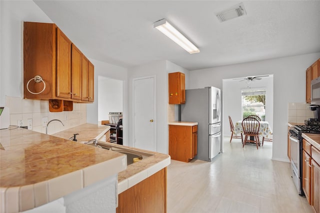 kitchen featuring ceiling fan, sink, stainless steel appliances, kitchen peninsula, and decorative backsplash