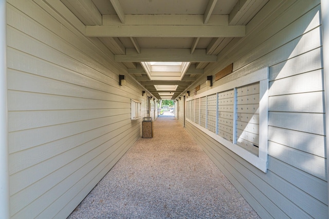 hall featuring carpet flooring, wood walls, and beamed ceiling