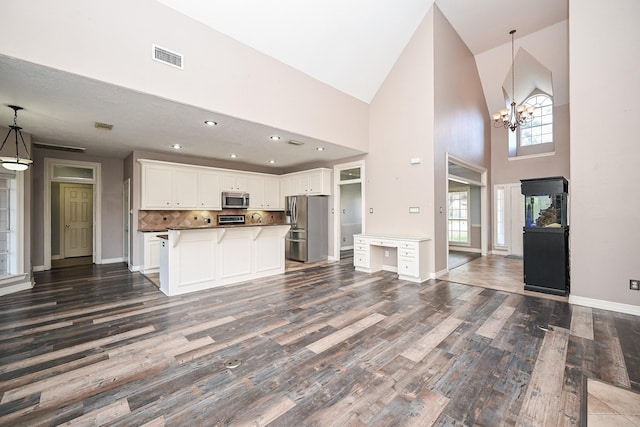 kitchen featuring high vaulted ceiling, white cabinets, appliances with stainless steel finishes, tasteful backsplash, and decorative light fixtures