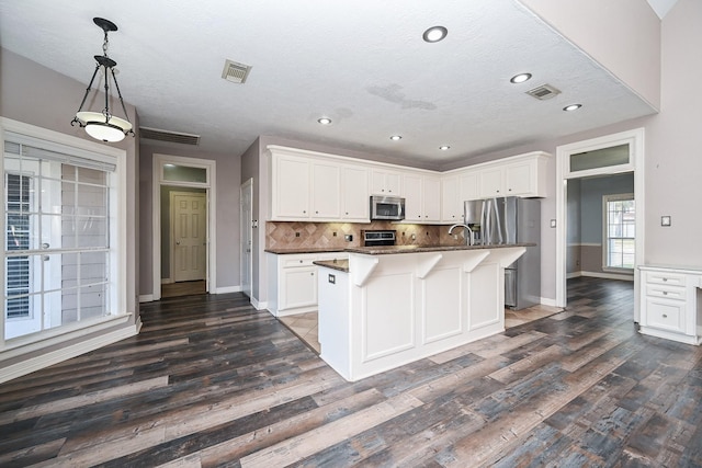 kitchen featuring a center island with sink, decorative backsplash, white cabinetry, and stainless steel appliances