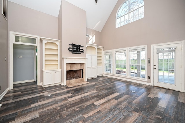 unfurnished living room featuring built in shelves, a premium fireplace, a towering ceiling, and dark hardwood / wood-style floors