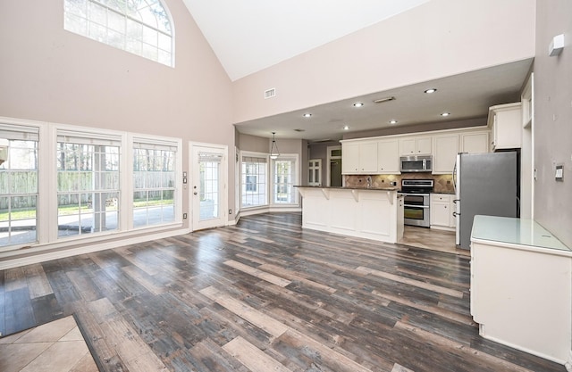 kitchen with stainless steel appliances, tasteful backsplash, a kitchen breakfast bar, high vaulted ceiling, and a kitchen island