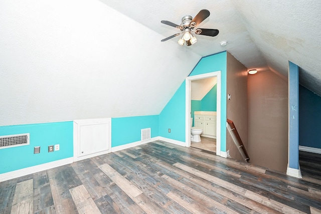 bonus room with a textured ceiling, ceiling fan, dark wood-type flooring, and vaulted ceiling