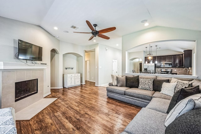 living room with ceiling fan, wood-type flooring, a fireplace, and vaulted ceiling