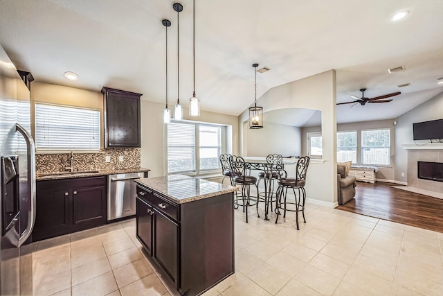 kitchen with dark brown cabinetry, lofted ceiling, appliances with stainless steel finishes, and a tiled fireplace