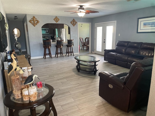 living room with ceiling fan, french doors, light hardwood / wood-style floors, and a textured ceiling