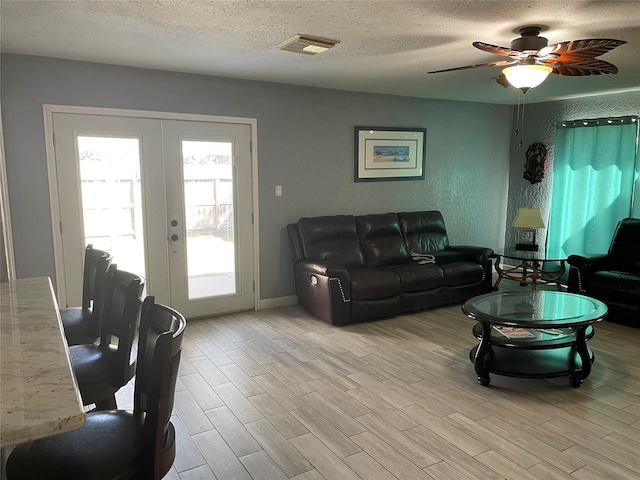 living room featuring light wood-type flooring, french doors, a textured ceiling, and ceiling fan