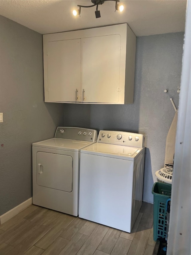 clothes washing area with cabinets, a textured ceiling, and washing machine and clothes dryer