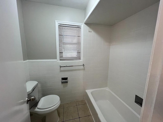 bathroom featuring tile patterned floors, a bath, toilet, and tile walls