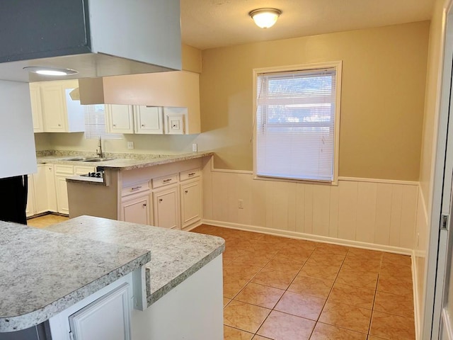 kitchen with kitchen peninsula, sink, white cabinets, and light tile patterned floors