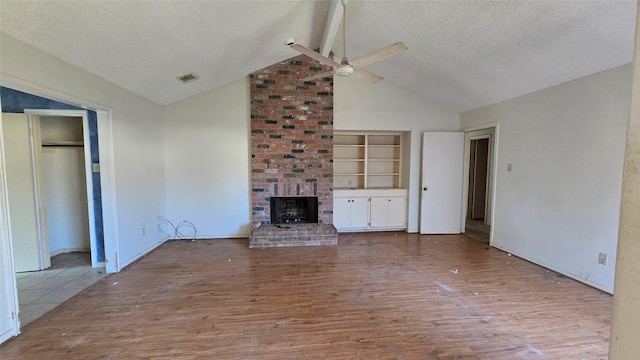 unfurnished living room featuring built in features, lofted ceiling with beams, a textured ceiling, and light wood-type flooring