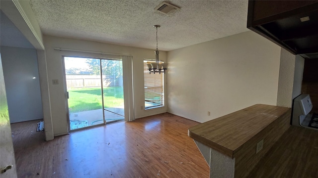 unfurnished dining area with a chandelier, a textured ceiling, and wood-type flooring