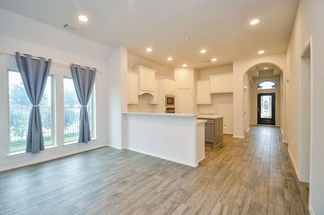 kitchen with built in microwave, white cabinetry, a center island, kitchen peninsula, and light wood-type flooring