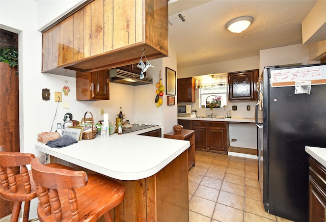 kitchen with sink, a kitchen breakfast bar, black fridge, kitchen peninsula, and a textured ceiling