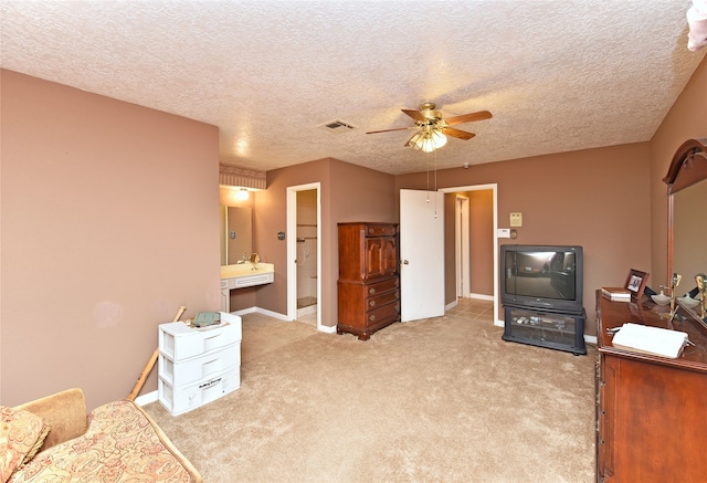 bedroom with a textured ceiling, connected bathroom, light colored carpet, and ceiling fan