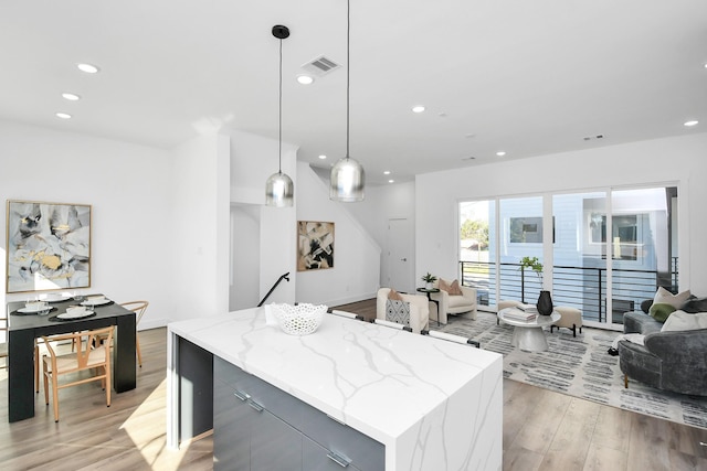 kitchen with pendant lighting, a center island, gray cabinets, light stone countertops, and light wood-type flooring