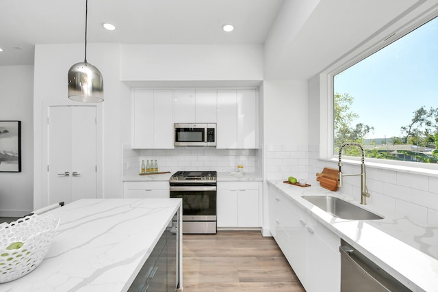 kitchen with light stone countertops, appliances with stainless steel finishes, sink, white cabinetry, and hanging light fixtures