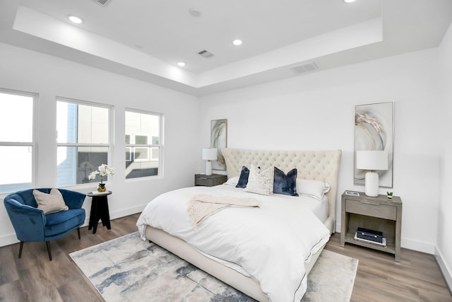 bedroom with wood-type flooring and a tray ceiling