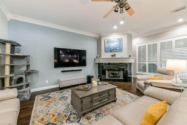 living room featuring ceiling fan, dark hardwood / wood-style flooring, ornamental molding, and a tile fireplace