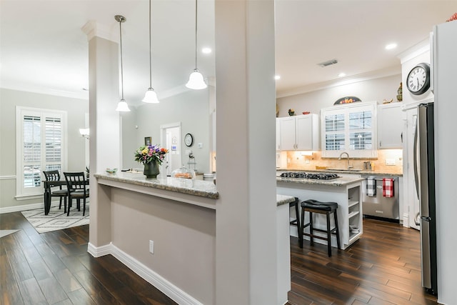 kitchen with light stone countertops, a kitchen breakfast bar, stainless steel appliances, pendant lighting, and white cabinets