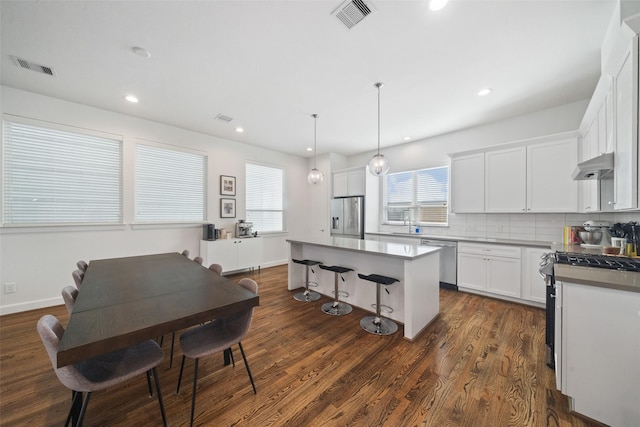 kitchen with a center island, backsplash, decorative light fixtures, white cabinetry, and stainless steel appliances