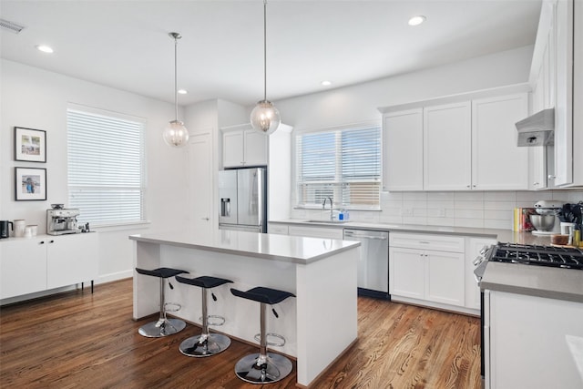 kitchen featuring sink, stainless steel appliances, a kitchen island, white cabinets, and exhaust hood