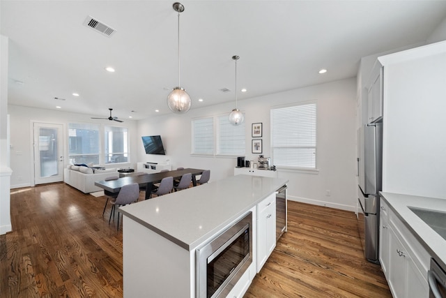 kitchen with pendant lighting, a center island, ceiling fan, appliances with stainless steel finishes, and white cabinetry