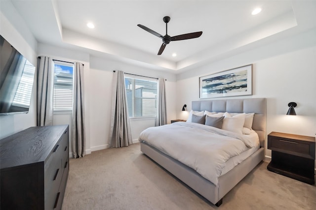 carpeted bedroom featuring a tray ceiling, multiple windows, and ceiling fan