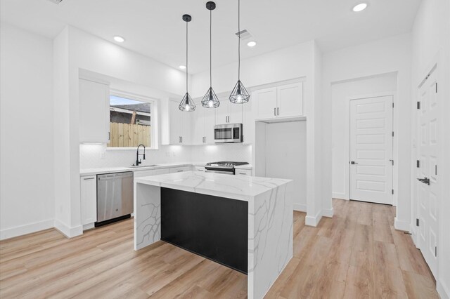 kitchen with light stone counters, stainless steel appliances, white cabinets, a kitchen island, and hanging light fixtures