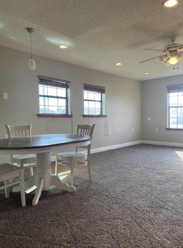 dining room with ceiling fan, a healthy amount of sunlight, a textured ceiling, and dark colored carpet