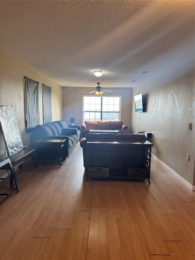 living room with ceiling fan, a textured ceiling, and light wood-type flooring