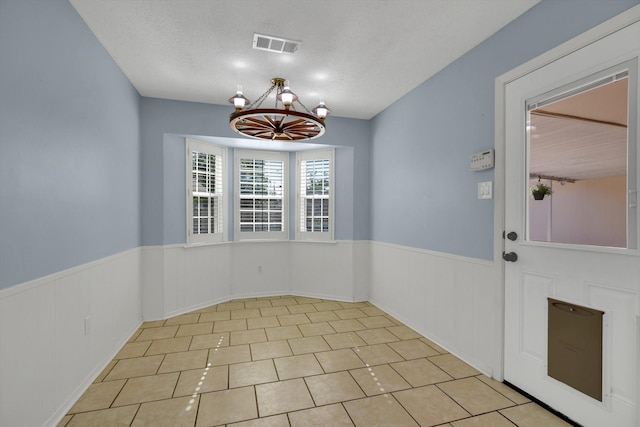 unfurnished dining area with light tile patterned floors, a textured ceiling, and an inviting chandelier