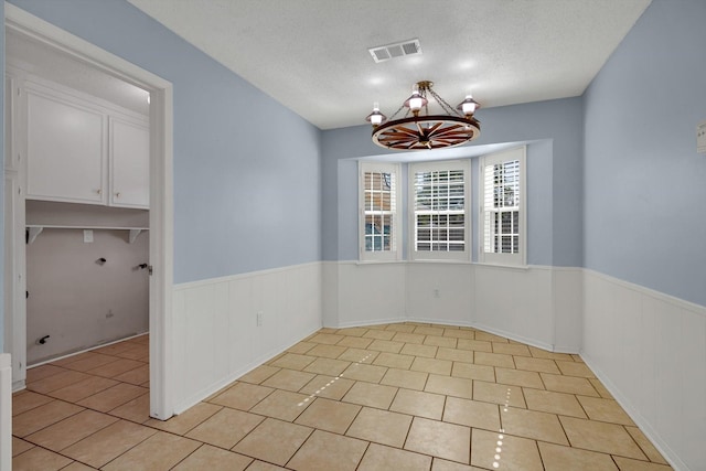 unfurnished dining area with light tile patterned floors, a textured ceiling, and an inviting chandelier