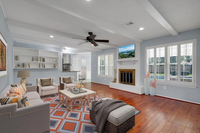 living room with beam ceiling, dark hardwood / wood-style flooring, a textured ceiling, and a brick fireplace