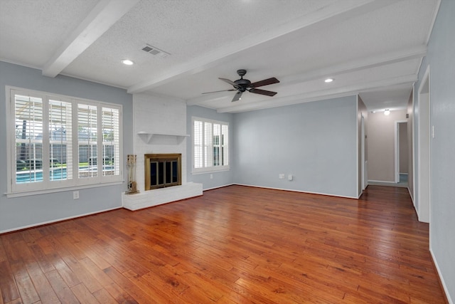 unfurnished living room with a fireplace, beam ceiling, a textured ceiling, and hardwood / wood-style floors