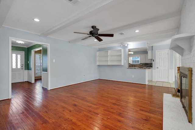 unfurnished living room featuring beamed ceiling, ceiling fan, hardwood / wood-style floors, and a brick fireplace