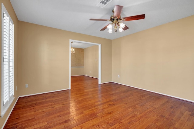 empty room featuring hardwood / wood-style floors, ceiling fan with notable chandelier, and plenty of natural light