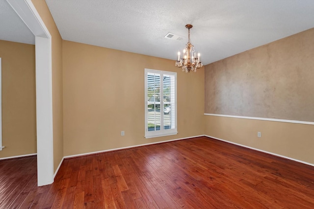 spare room with a textured ceiling, hardwood / wood-style flooring, and an inviting chandelier