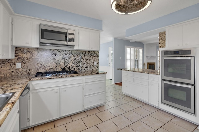 kitchen featuring decorative backsplash, light stone countertops, stainless steel appliances, light tile patterned floors, and white cabinetry