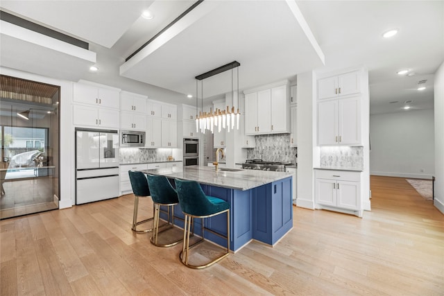 kitchen with a center island with sink, appliances with stainless steel finishes, white cabinets, light stone counters, and sink