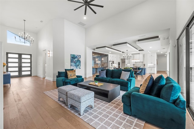 living room with ceiling fan with notable chandelier, a high ceiling, light hardwood / wood-style flooring, and french doors