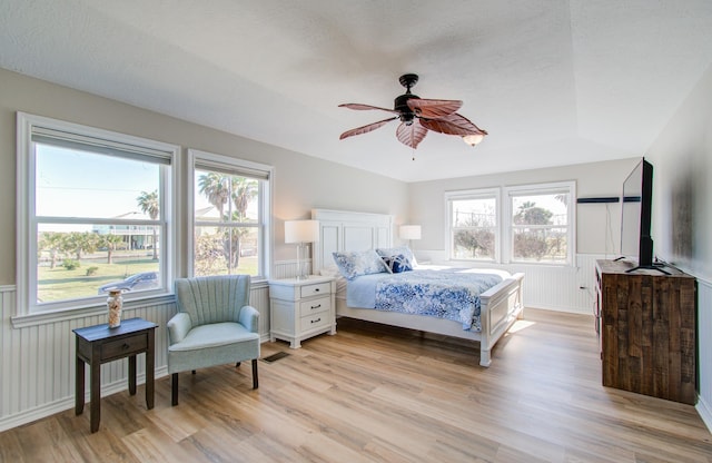 bedroom with light wood-style flooring, visible vents, and a wainscoted wall