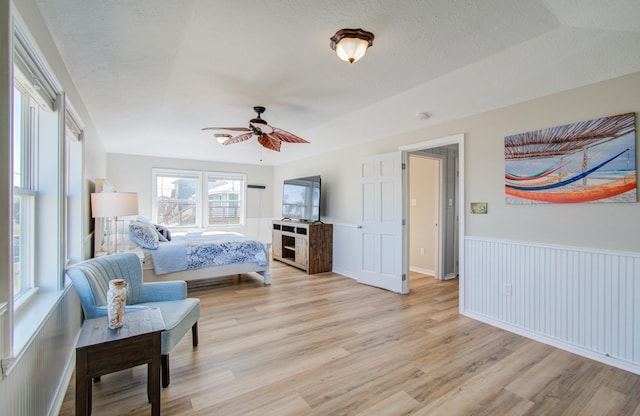 bedroom featuring a textured ceiling, ceiling fan, light wood-type flooring, and wainscoting