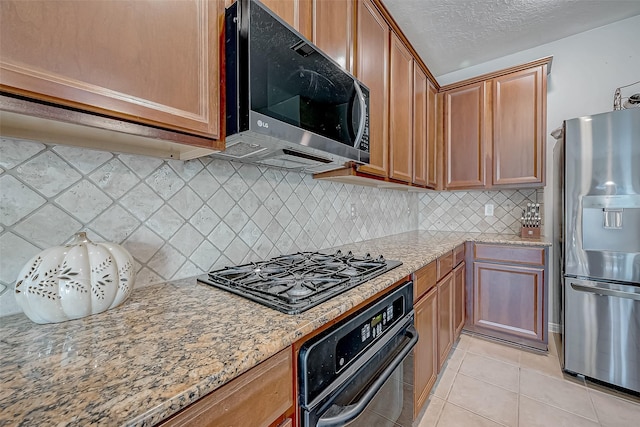 kitchen with a textured ceiling, light tile patterned floors, tasteful backsplash, light stone countertops, and black appliances