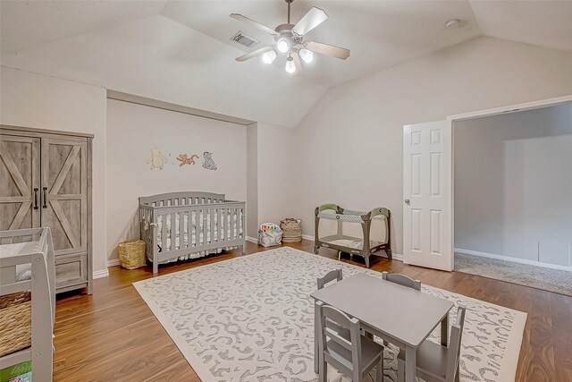 bedroom with ceiling fan, lofted ceiling, a nursery area, and wood-type flooring