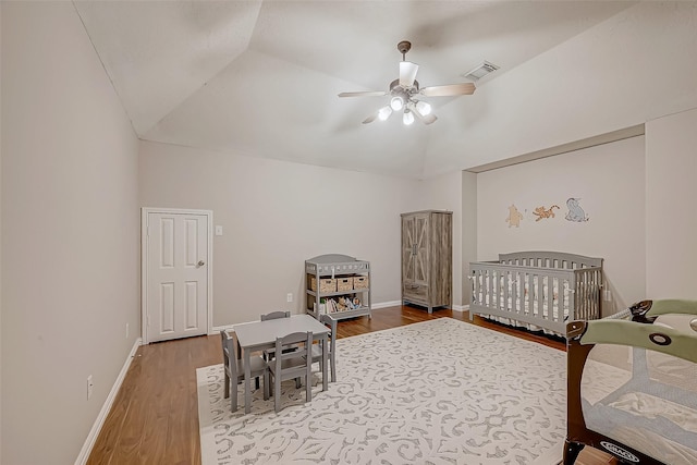 bedroom with lofted ceiling, ceiling fan, a crib, and hardwood / wood-style floors