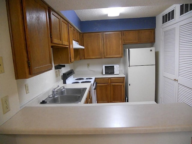 kitchen featuring a textured ceiling, kitchen peninsula, white appliances, and sink