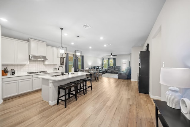 kitchen featuring white cabinetry, ceiling fan, hanging light fixtures, stainless steel gas cooktop, and an island with sink