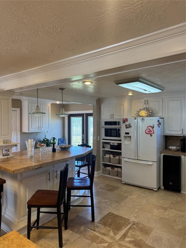 kitchen featuring white cabinetry, white fridge with ice dispenser, stainless steel oven, hanging light fixtures, and ornamental molding